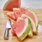 Eight slices of watermelon in a wedge shape on a cutting board with a knife.